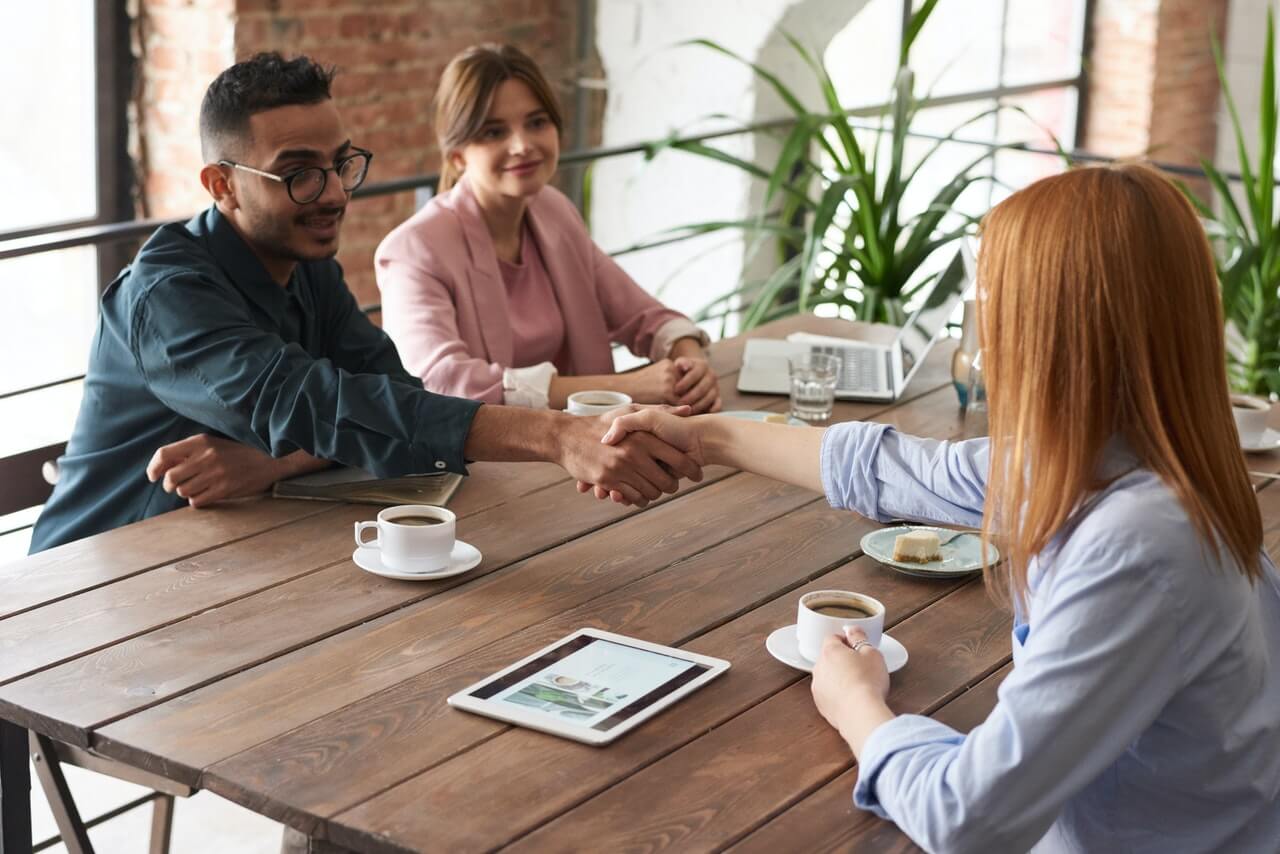 three people sitting at a table having a professional meeting, two of them are shaking hands